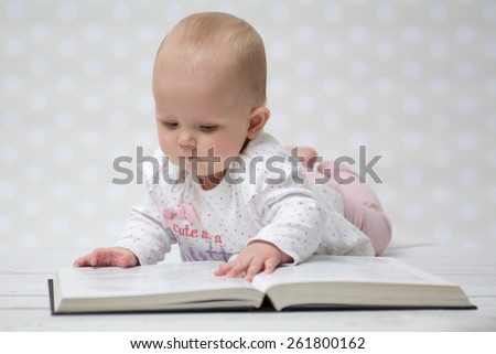 Baby girl lying on the belly reading a book