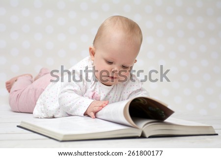 Baby girl lying on the belly reading a book