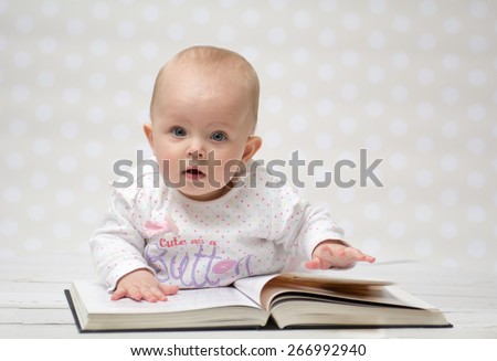 Baby girl lying on the belly reading a book and looking at the camera