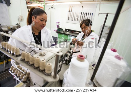 CAPE TOWN, SOUTH AFRICA - AUG 2: Women work with white thread for new garments in a large clothing factory in Cape Town, South Africa on August 2, 2012