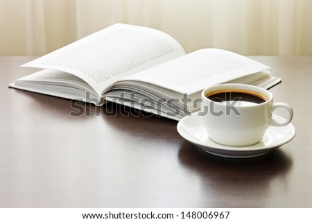 Cup of coffee and opened book on table against window