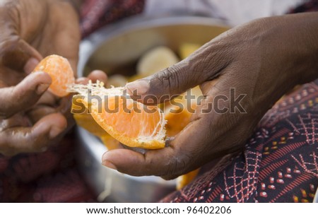 Hands of Indian woman peeling tangerine for fruit salad