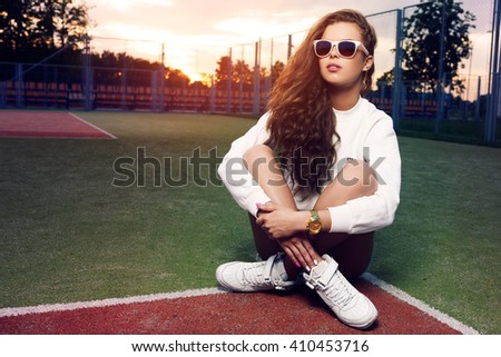 Beautiful young girl in sunglasses on the tennis court. Beautiful healthy hair. Denim shorts. White sneakers