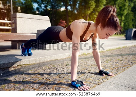 Young beautiful and strong woman doing push-ups in the park in the summer. Sports concept. Healthy lifestyle