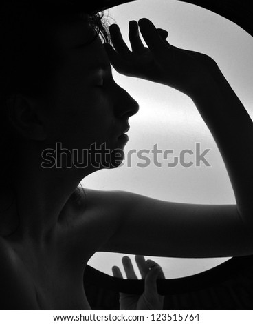 girl\'s face and arms sillhouette holding circle of light. black and white portrait