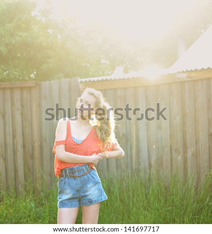 portrait photo of beautiful girl in summer light standing near fence