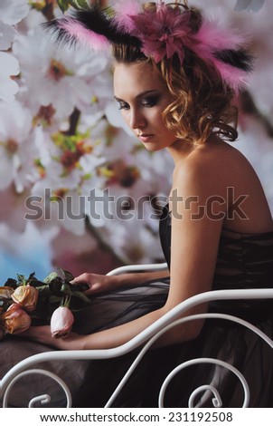 portrait photo of beautiful girl with feathers in hair sitting on bed holding roses