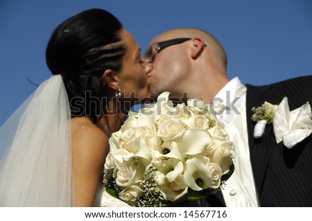 Bride and groom is kissing while showing the bouquet. The focus is on the flowers the couple are in blur
