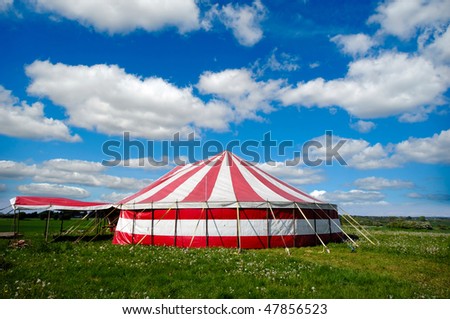 A red and white striped circus tent in green nature. The sky is blue with white cumulus clouds