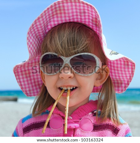 A funny little girl in sunglasses and a hat, with two salty sticks in the mouth