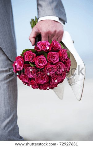 Groom holding wedding flowers and shoes on the beach