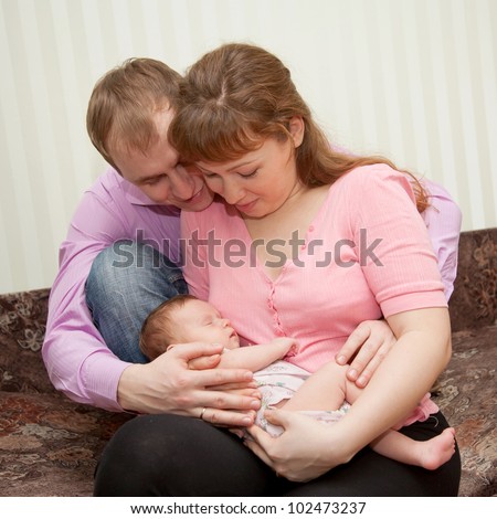 Happy beautiful young family with a newborn baby sitting. Father and Mother hugging, holding a baby. The symbol of family happiness