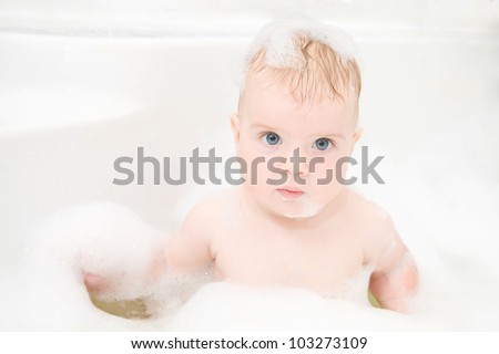 Cute baby boy with blond hair and blue eyes is washing hair hair and body in bath. The symbol of purity and hygiene education