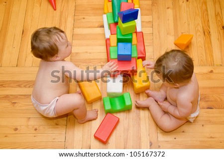Two lovely baby twins are building houses of  colorful cubes and toy blocks