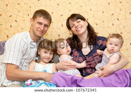 Happy smiling young big family, five people - mother, father, big daughter and two twins small baby girls. The family is sitting at home on the sofa. Happy family concept