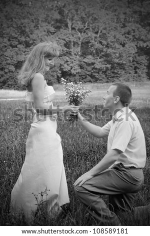 Black and white portrait of the loving couple on the lawn. Gentleman presents lady flowers. Retro style.