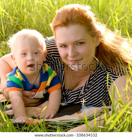 Happy mother and baby with Down syndrome are lying on the grass in the park. Summer holiday.