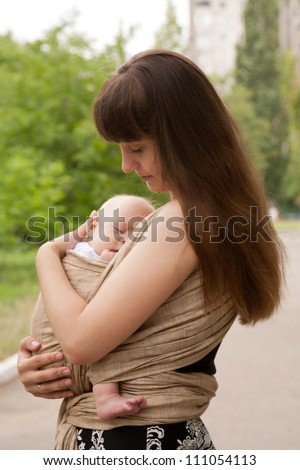 Best deep sleep. Newborn baby sleeping in a sling, in the embrace of young mother