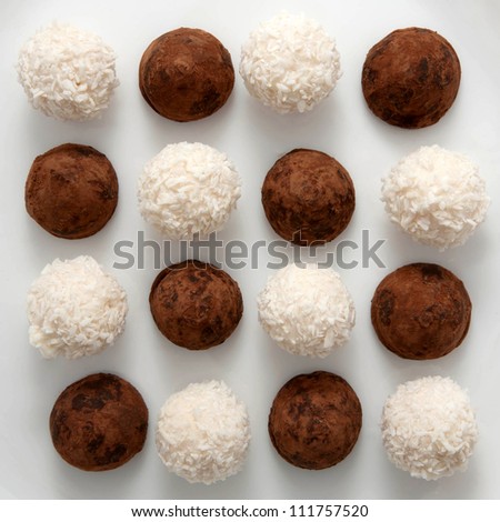 Dark chocolate truffles sprinkled with cocoa and white truffles, sprinkled in coconut chips, are staggered. Sweet candy black and white background