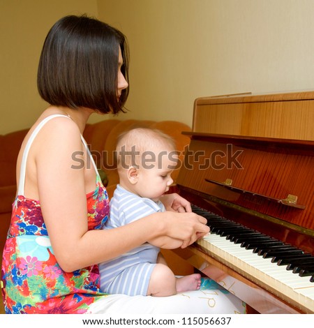 Baby is learning to play the piano. Mother helping him