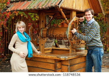 Young pregnant couple in love  posing in an old wooden well in the village