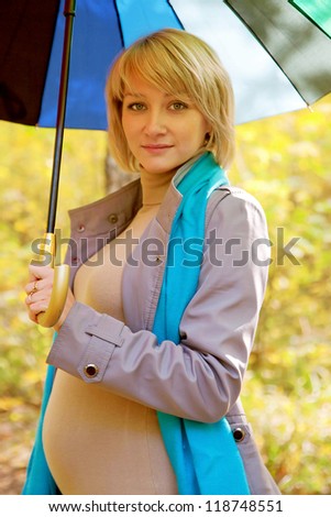 Happy pregnant woman in the autumn forest under a rainbow colorful umbrella
