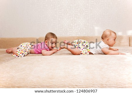 Two baby twins crawling one after another on the sofa