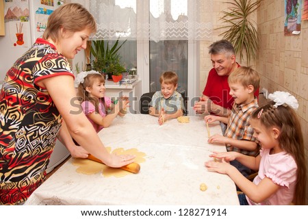 Happy big family cooking a pie together. Father, mother and four children, two boys and two girls playing with dough in the kitchen.