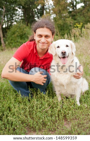 Smiling man hugging a dog breed golden retriever on green grass in the park.