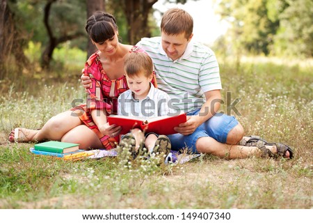 Happy father, mother and son reading book on the lawn in the park. Family reading together. Summer holiday. Happy family concept.