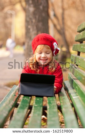 Happy smiling little girl using tablet outdoors.  Computer generation concept.