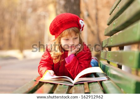 Happy smiling little girl reading interesting book in the park.
