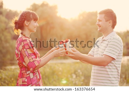 Man giving to his woman a gift box Happy middle-aged couple in love outdoors in the sunlight at sunset Love concept Retro style Man giving to his woman a gift box Happy middle-aged couple in love outdoors in the sunlight at sunset Love concept Retro style