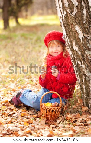 Happy smiling little girl with a basket filled with mushrooms in the autumn forest. Harvest concept.