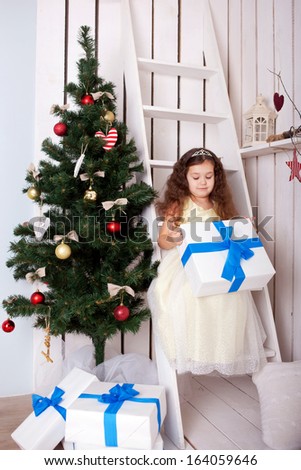 Happy elegant little girl holding gifts near the Christmas tree. Christmas, New Year, holiday concept, ready for your text, logo, letters or symbols.