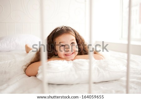 Pretty little girl waking up in the morning. Dream the little princess on a white bed close-up.