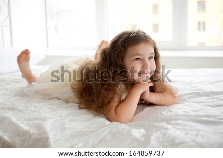Happy smiling child waking up in the morning. Dream the little princess on a white bed close-up.