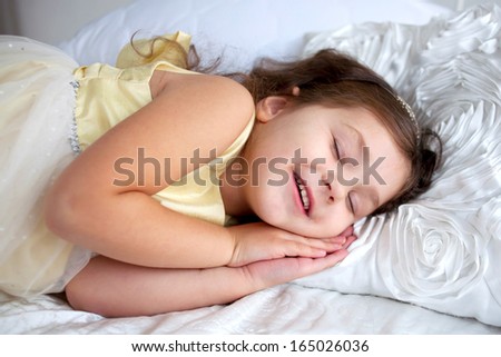 Happy smiling kid sleeping and smiling in her sleep. Dream the little princess on a white bed close-up.