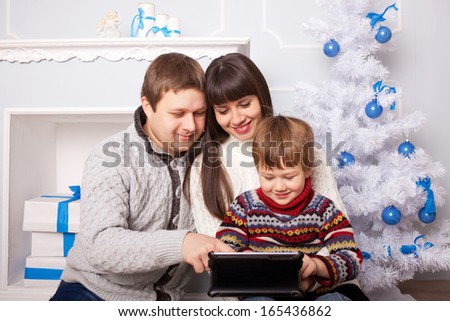 Happy family using the tablet near the fireplace and Christmas tree. Funny father, mother and child, smiling family with tablet pc looking at something and laughing. Happy family concept.