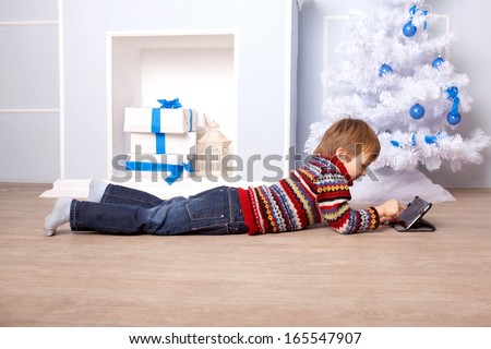 Happy child using a tablet PC near the Christmas tree and fireplace. Computer Generation concept.
