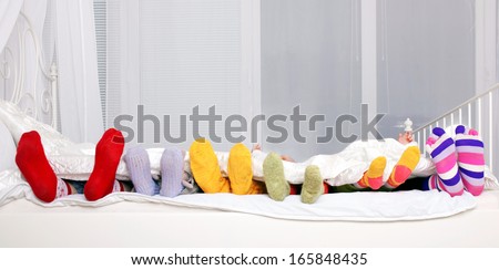 Happy family concept. Feet of father, mother and four children in colorful knitted socks on white bed. Family sleeping together.