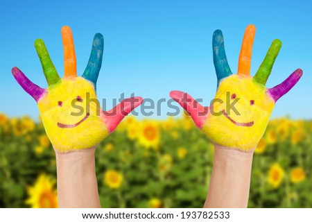 Two smiley hands on a background of field of sunflowers  and blue sky in sunny summer's day. Summer holidays concept.