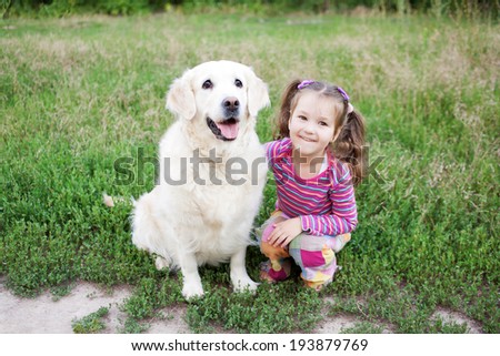 Happy small child hugging a dog breed golden retriever on green grass in the park.