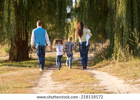 Big happy family walking on the road in the park. Father, mother, son, daughter and baby holding hands and going together. Rear view. Family Ties concept.