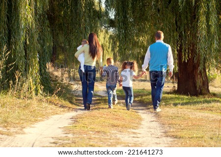Big happy family walking on the road in the park. Father, mother, son, daughter and baby holding hands and going together. Rear view. Family Ties concept.