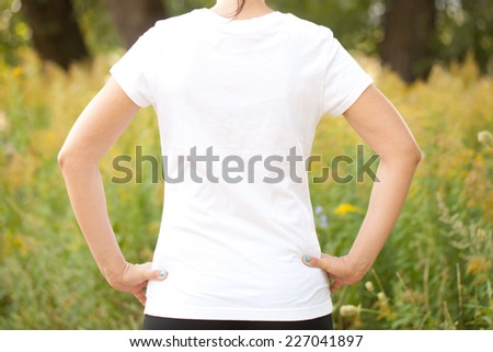 Young woman in white t-shirt outdoors. Ready for your text or symbol. Rear view.
