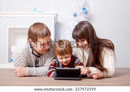 Happy family using the tablet near the fireplace and Christmas tree.