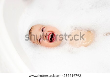 Funny cute baby is swimming in foam in the bath