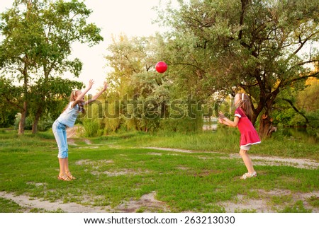 Kids playing in a suburban neighborhood. Two sisters or girlfriends throwing the ball to each other.