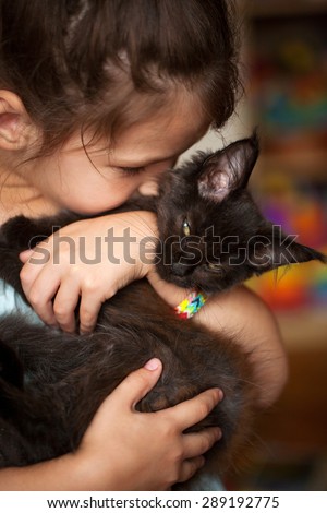 Little girl hugging and kissing a black kitten Maine Coon